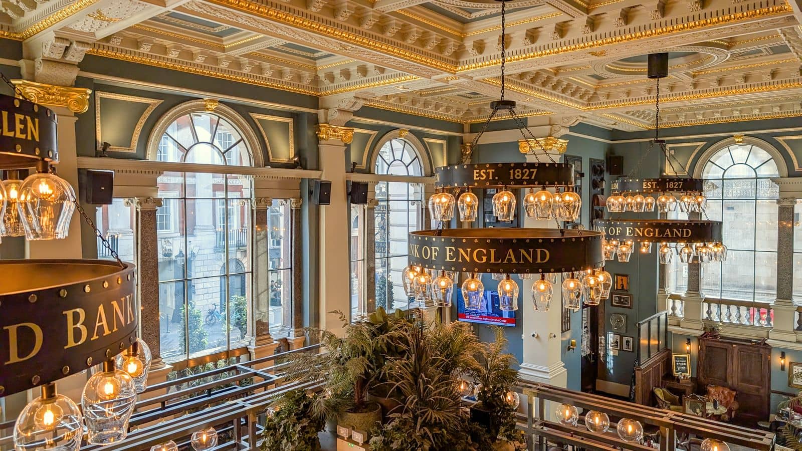 The ornate interior of a former bank hall with chandeliers and a gallery