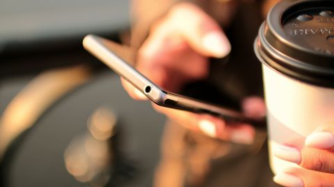 A person scrolling on a smartphone while holding a takeaway coffee