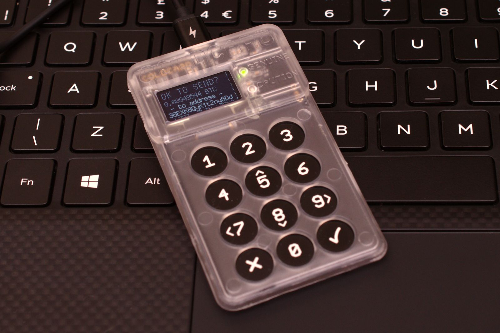 A transparent hardware wallet with a number pad lying on a laptop keyboard