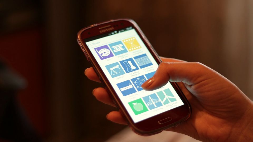A hand holding a smartphone with app tiles on the screen
