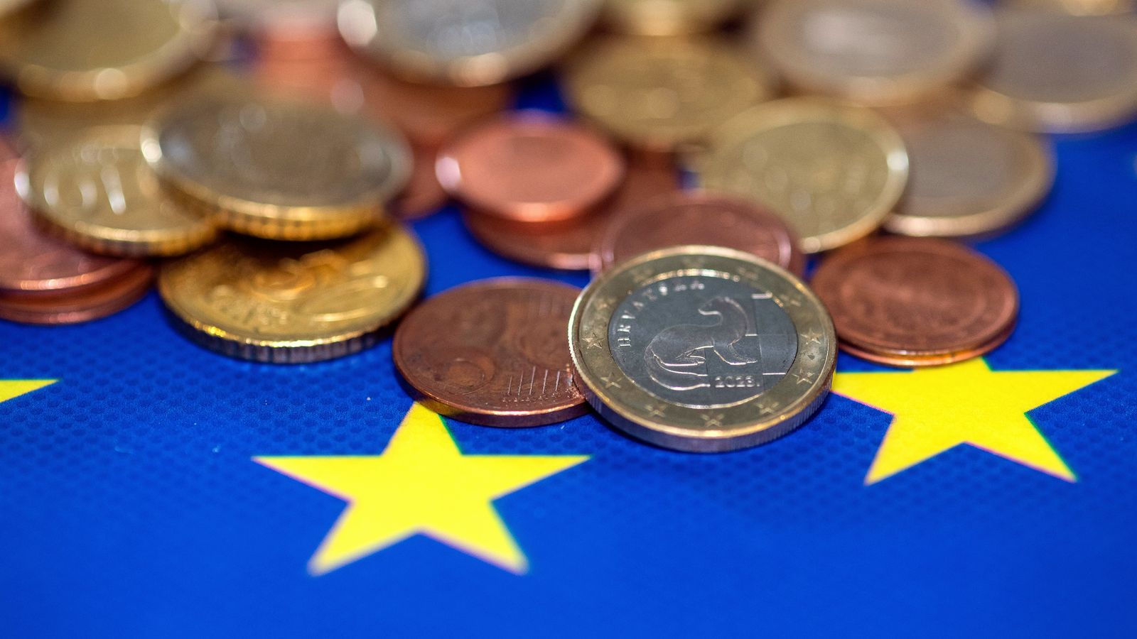 Euro coins piled on a blue flag with yellow stars