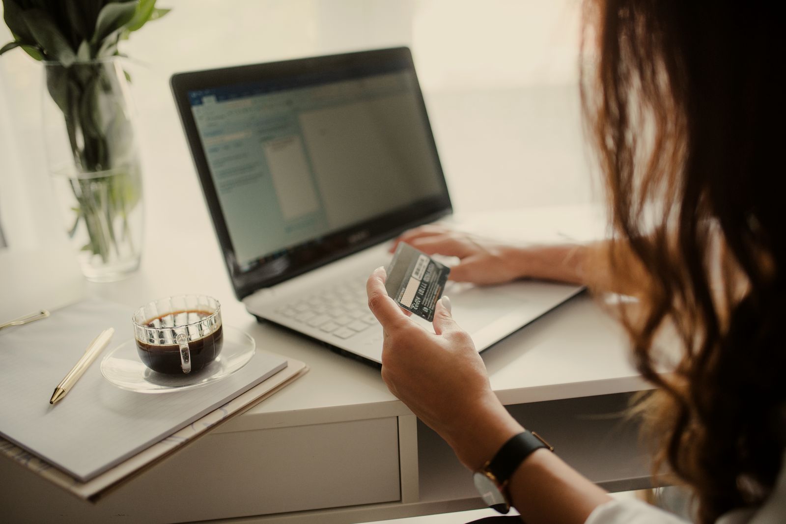 A person holding a payment card while using a laptop at a desk
