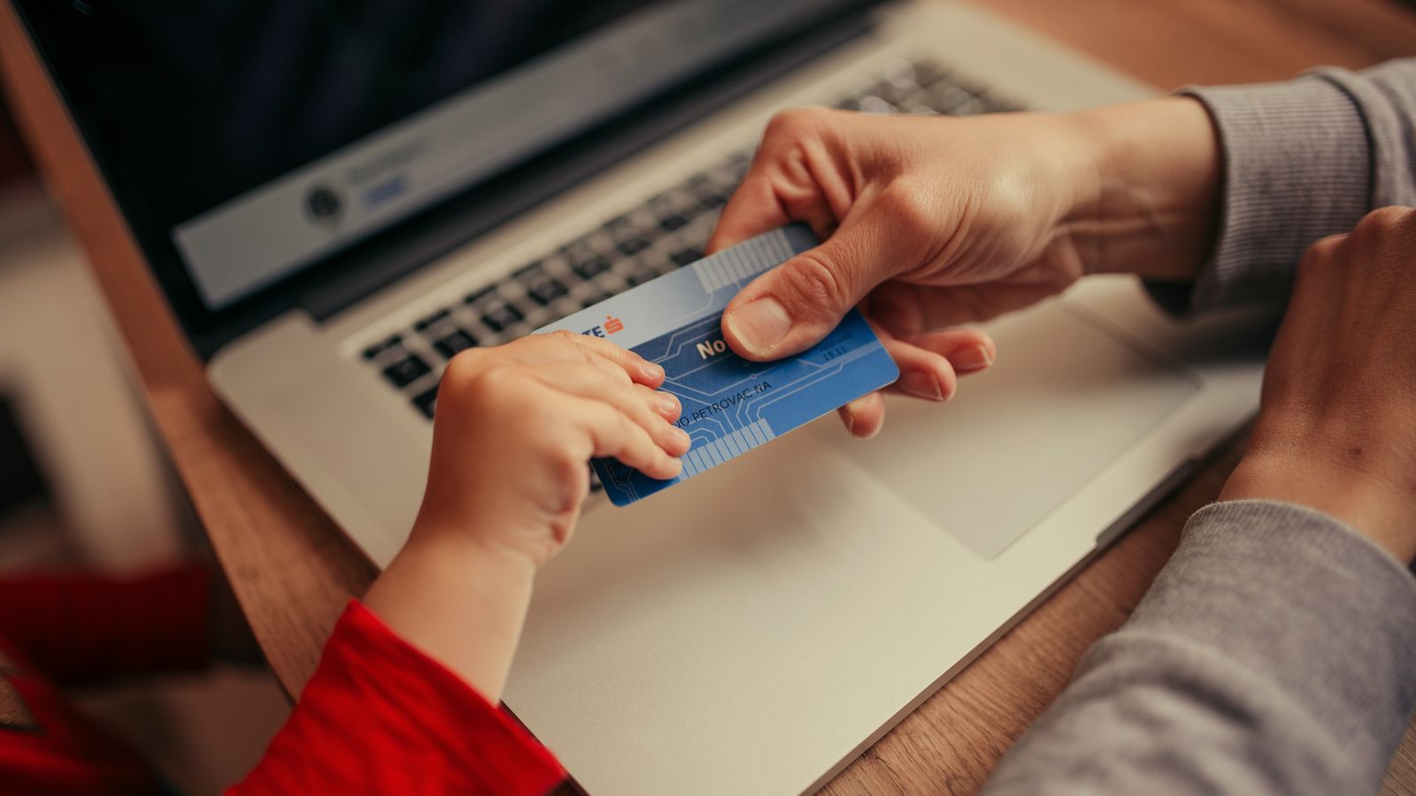 Hands holding a payment card above a laptop keyboard while shopping online