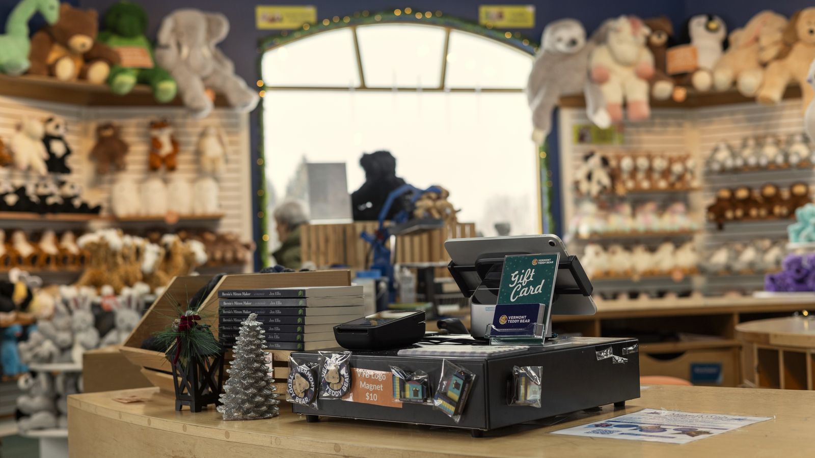 A shop checkout counter with a card terminal and till, surrounded by teddy bears