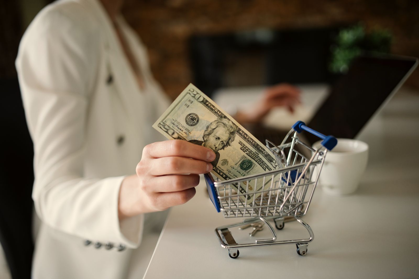 A hand dropping a banknote into a miniature shopping trolley