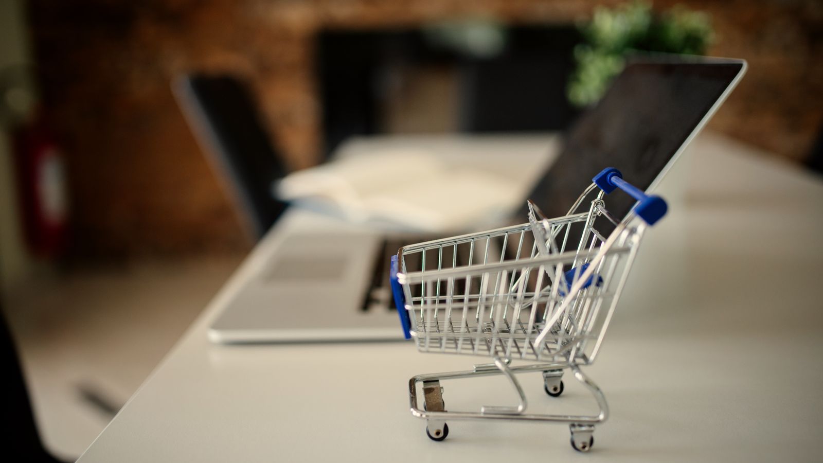 A miniature shopping trolley on a desk next to a laptop