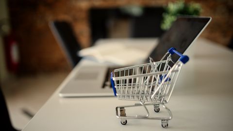 A miniature shopping trolley on a desk next to a laptop