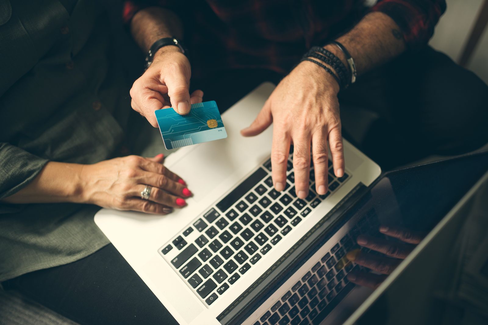 Hands holding a payment card over a laptop keyboard