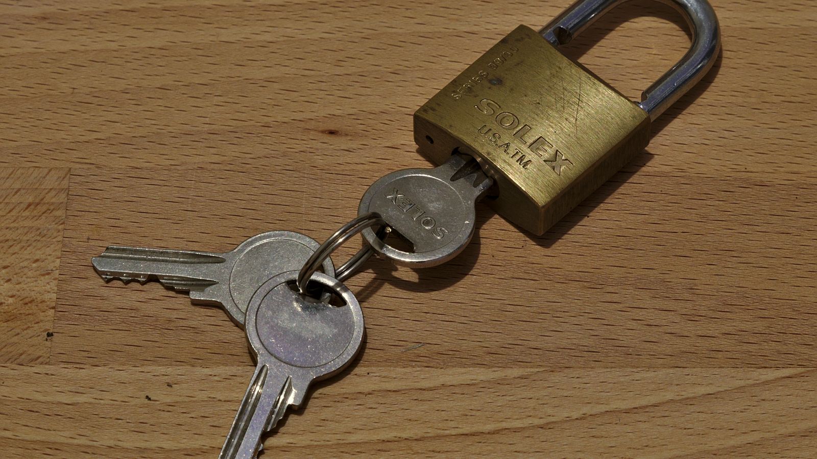 An open brass padlock with its keys on a wooden table