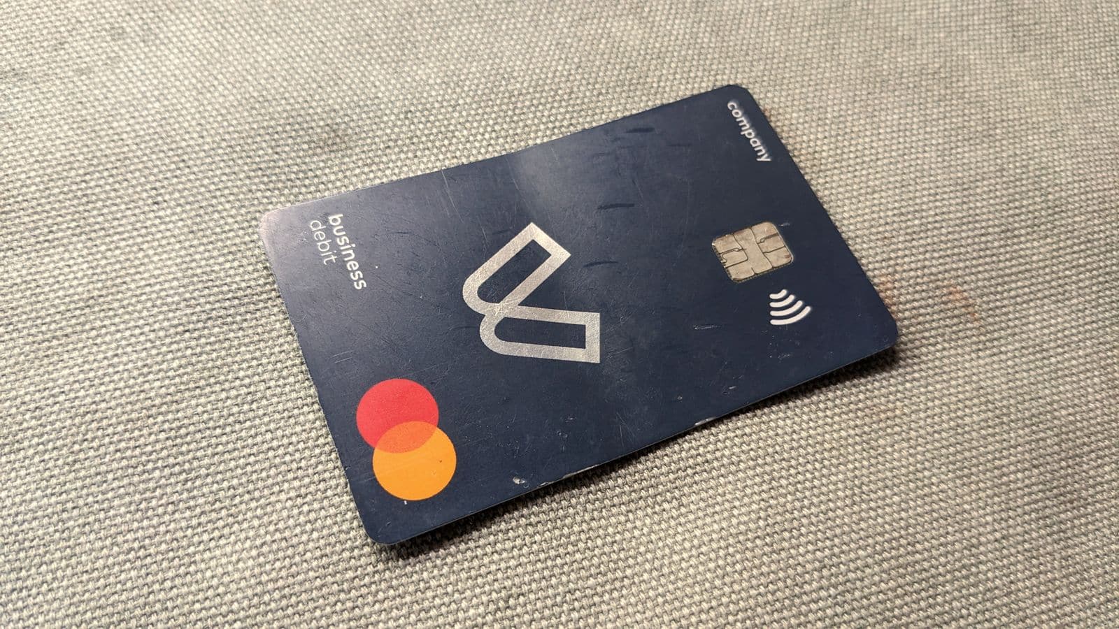 A contactless business debit card with the Mastercard mark lying on grey fabric