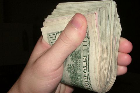 A hand gripping a thick wad of US dollar bills
