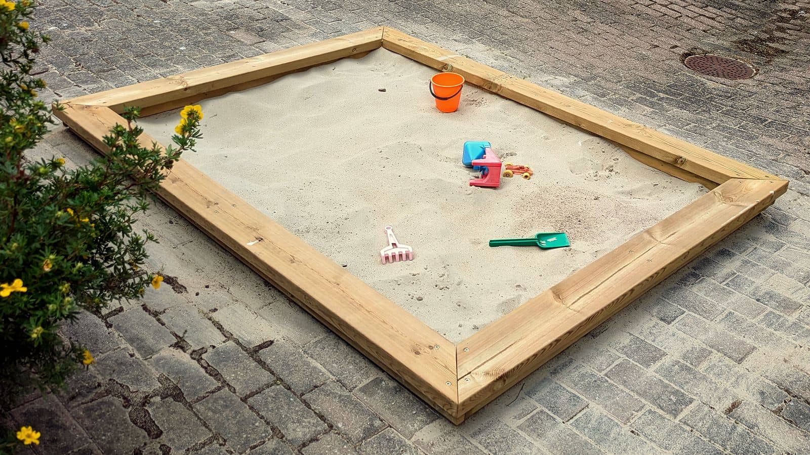 A wooden-framed sandbox with a few children's toys in the sand
