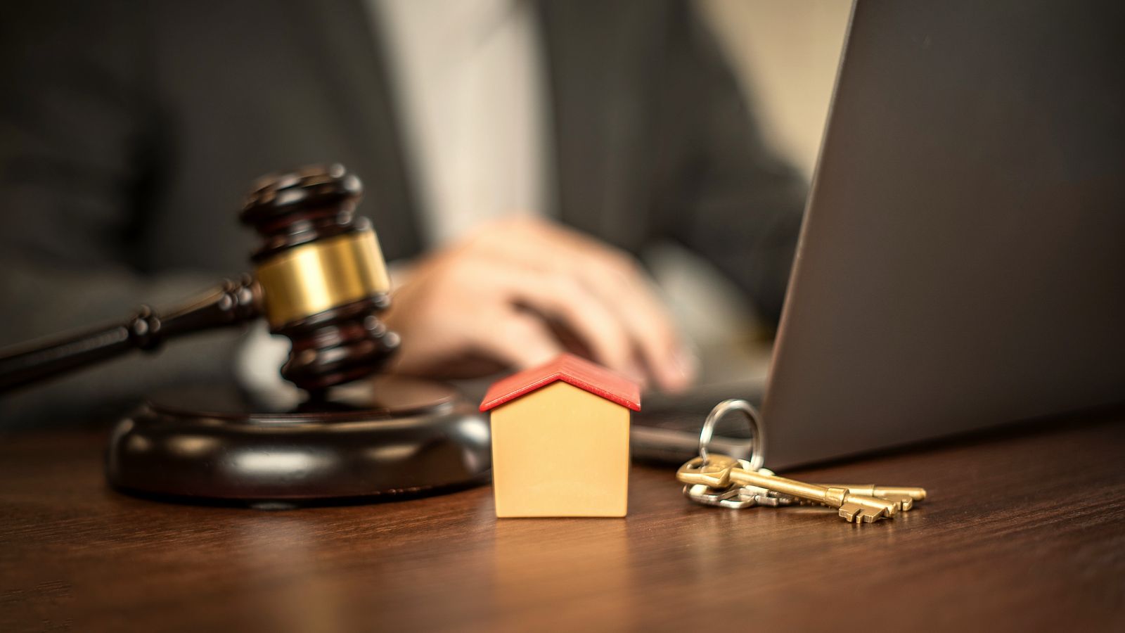 A judge's gavel, a toy house and a set of keys beside a laptop