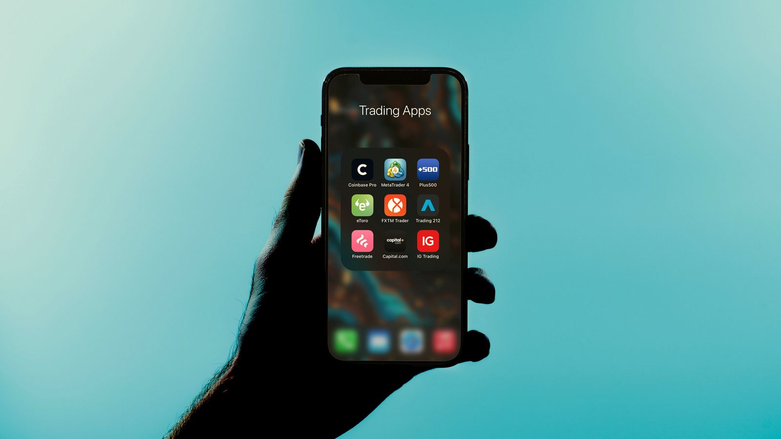 A hand holding a phone that shows a folder of investing apps