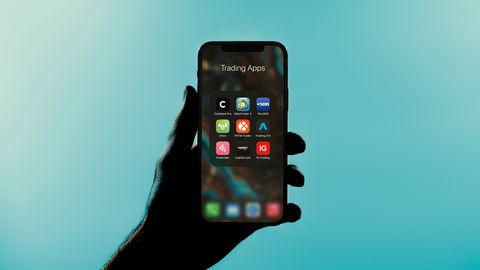 A hand holding a phone that shows a folder of investing apps